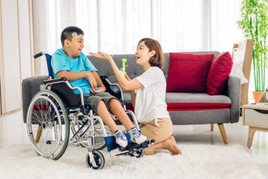 Mutlu aşk portresi. Asyalı anne oynuyor ve bakıcı tekerlekli sandalyede oturan engelli çocuğa bakıyor. Evde engelli bakımı konseptinde iyi vakit geçiriyor.