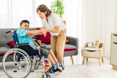 Mutlu aşk portresi. Asyalı anne oynuyor ve bakıcı tekerlekli sandalyede oturan engelli çocuğa bakıyor. Evde engelli bakımı konseptinde iyi vakit geçiriyor.