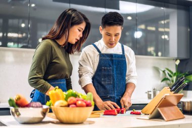 Genç Asyalı çift taze sebzelerle yemek yaparken eğleniyor. Masada sağlıklı yiyecekler. Mutlu çift, mutfakta lezzetli yemekler hazırlıyor.