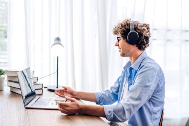 Evde dizüstü bilgisayarla çalışan ve video konferansı yapan gülümseyen genç adam. Ev konseptinden ekran daktilo mesajına bakan genç yaratıcı adam.