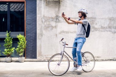Sırt çantalı yakışıklı bir adamın portresi akıllı telefon ile internetteki GPS haritasını kontrol ederek bisiklet sürerek işe gidiyor. İş seyahati teknolojisi kavramı.