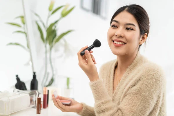 Smiling of young beautiful pretty asian woman clean fresh healthy white skin.asian girl holding make-up brushes and make up on face with cosmetics set at home.facial beauty
