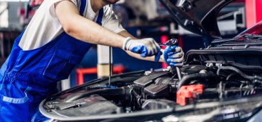 Üniformalı profesyonel araba teknisyeni araba motoru tamiri ve oto servisindeki araba kaputunun altındaki onarım onarım işlerini yapıyor. Otomobil servisi garajı