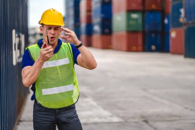 Kasklı profesyonel mühendis konteynır ustabaşı ayakta çalışıyor ve telsiz kullanıyor. Stokları yükleme için konteynıra koyuyor. Lojistik ulaşım ve iş sektörü ihracatı
