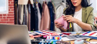 Genç, güzel Asyalı kadın moda tasarımcısının portresi. Renk örnekleriyle çalışıyor. Moda stüdyosunda renkli kumaşlarla çalışan genç Asyalı kız.