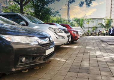 Birçok araç toplum yolundaki ağaçların altında arka arkaya dizilmiş durumda. Araba satıcısı arabaları satılık halde tutardı.