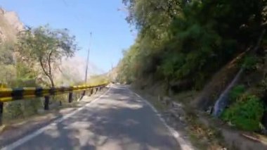 Empty long mountain rural road of National Highway 34 connecting Uttarkashi - Gangotri Road on the way to Harsil. POV of car driving on highway road Surrounded by forests.