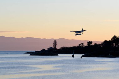 A seaplane on final approach to land in the harbour at Victoria, British Columbia, Canada during twilight or golden hour.