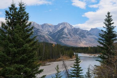 A landscape view of the Bow River valley in beautiful Banff National Park, Alberta, in the Canadian Rocky Mountains with deeply forested hills and blue sky with white clouds.