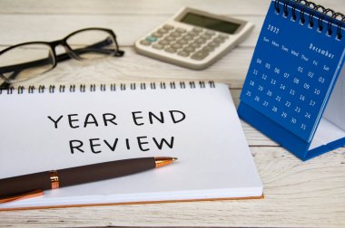 Not defterinde Aralık takvimi, gözlükler, hesap makinesi ve kalemle birlikte yıl sonu gözden geçirme metni. Yıl sonu kapanışı ve gözden geçirme kavramı.