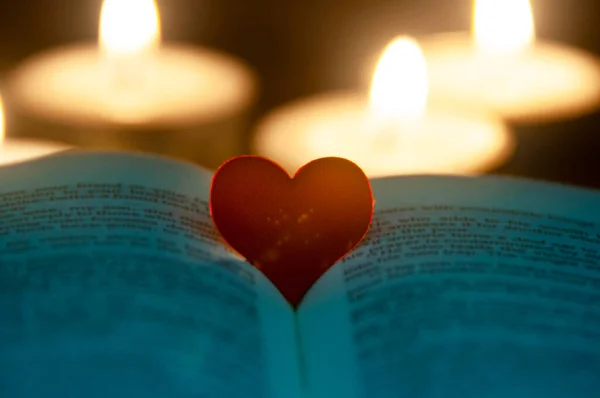 Red heart shape on Holy Bible with candle lights background. Customizable space for text or ideas. Copy space.
