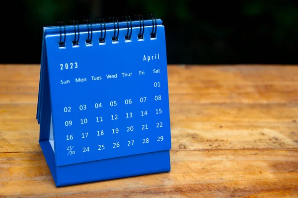 April 2023 blue desk calendar on wooden table background with customizable space for text.