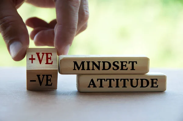 Hand turning wooden cube from negative to positive mindset and attitude text on wooden blocks.