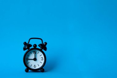 Alarm clock pointing at 9 am or pm with customizable space for text or ideas. Copy space with blue background.