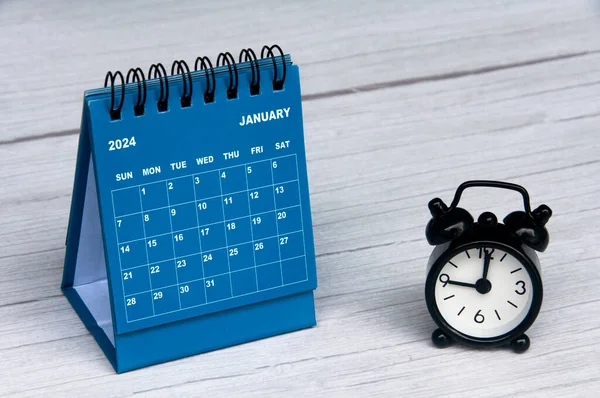 Stock image January 2024 calendar on wooden desk and alarm clock with customizable space for text. Monthly calendar concept and copy space