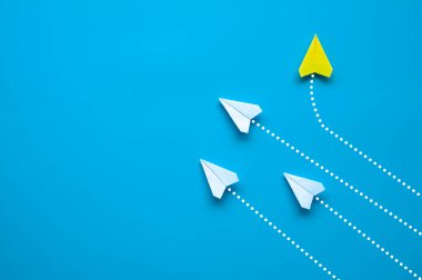Kağıt uçağın üst görüntüsü - Sarı kağıttan uçak origamisi farklı bir yöne uçuyor ve mavi arkaplanda diğer beyaz uçakları bırakıyor. Liderlik kavramı.