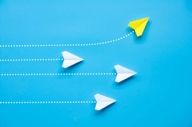 Kağıt uçağın üst görüntüsü - Sarı kağıttan uçak origamisi farklı bir yöne uçuyor ve mavi arkaplanda diğer beyaz uçakları bırakıyor.