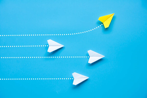 Top view of paper airplane - Yellow paper airplane origami flying to a different direction leaving other white airplanes on blue background.