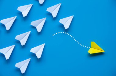 Sarı kağıttan uçak origamisi diğer beyaz uçakları mavi zemin üzerinde bırakır metin ya da fikirler için özelleştirilebilir alanla. Liderlik becerileri kavramı ve kopyalama alanı.