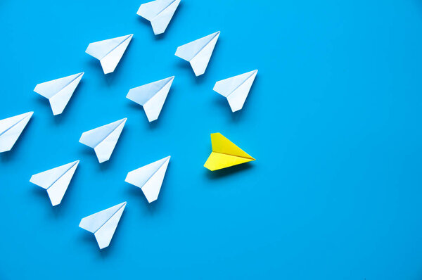 Yellow paper airplane origami leaving other white airplanes on blue background with customizable space for text or ideas. Leadership skills concept and copy space.