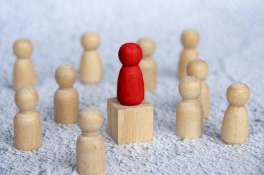 Tahta bloğun tepesindeki kırmızı tahta figür diğer ahşap figürlerle çevrili. Liderlik kavramı.