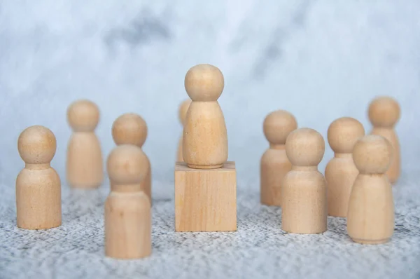 A wooden figure on top of wooden block representing a leader surrounded by other wooden figure. Leadership concept.