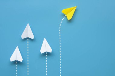 Sarı kağıttan uçak origamisinin üst görüntüsü mavi arka plandaki diğer beyaz uçaklardan farklı bir yöne uçuyor. Liderlik ve iş konsepti.