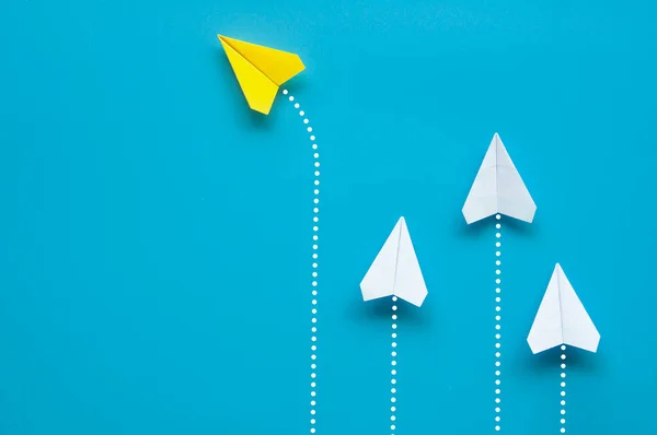 stock image Top view of yellow paper airplane origami flying to a different direction leaving other white airplanes on blue background. Leadership concept.