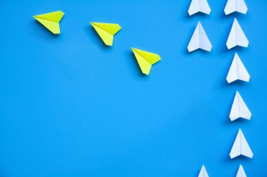 Üç sarı kağıttan uçak origamisi diğer beyaz uçakları mavi arkaplanda mesaj için özelleştirilebilir alanla bırakıyor. Liderlik becerileri kavramı.
