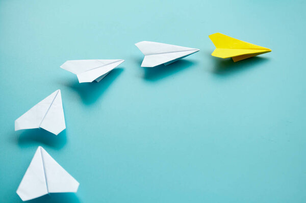Top view of yellow paper airplane origami leading other white paper airplanes with customizable space for text.