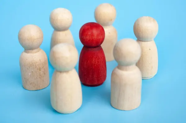 Red wooden figure surrounded with other wooden figure.