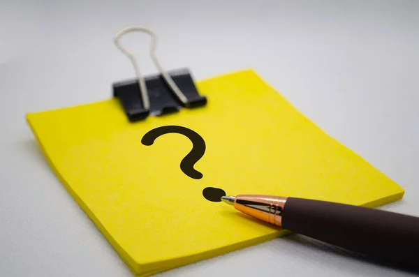 Close up of question mark on notepad with pen on white background. Question and answer concept.