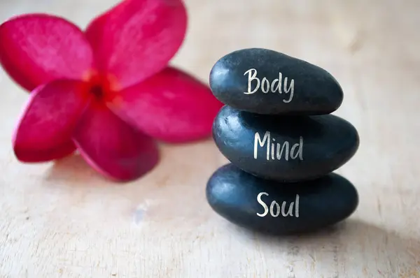 Body, Mind and Soul text engraved on black zen stones with red flower. Meditation and spa concept.