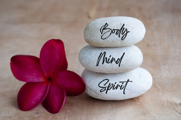 Body, Mind and Soul text engraved on white zen stones with red flower. Meditation and spa concept.