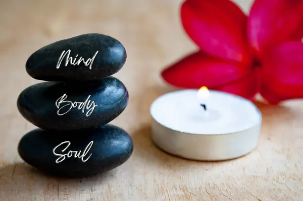 Mind, Body and Soul text engraved on black zen stones with candle. Meditation and spa concept.