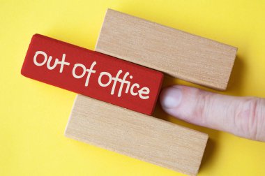 Sarı kapaklı ofis dışı metni olan kırmızı tahta bloğu iten parmak.