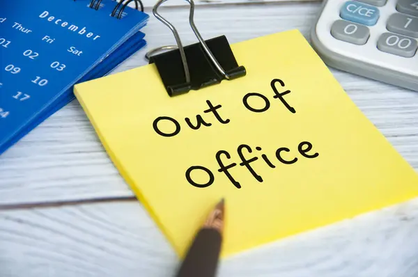 Out of office text on sticky notepad with December calendar and calculator background.