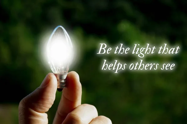 Motivational quote about being the light that helps others see with closeup light bulb background.