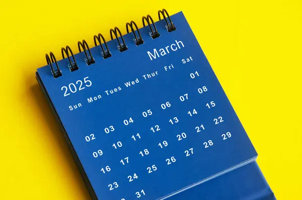 March 2025 blue desk calendar on yellow cover background. New month concept.