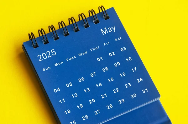 May 2025 blue desk calendar on yellow cover background. New month concept.