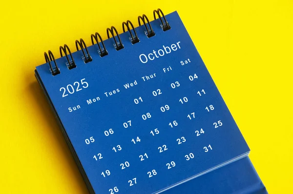 October 2025 blue desk calendar on yellow cover background. Calendar concept.
