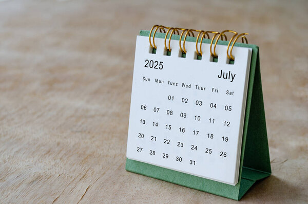 July 2025 table calendar on wooden desk with customizable space for text. Copy space and calendar concept.