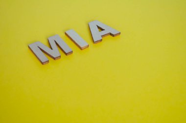 MIA wooden letters representing Missing In Action on yellow background. clipart