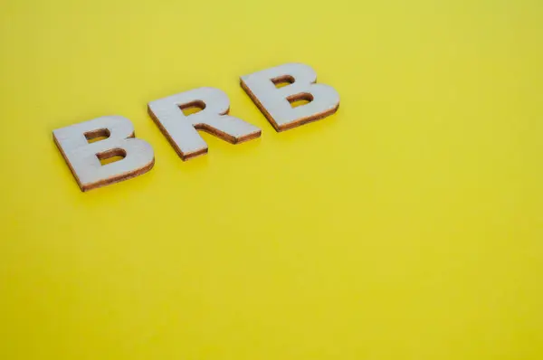 Stock image BRB wooden letters representing Be Right Back on yellow background.