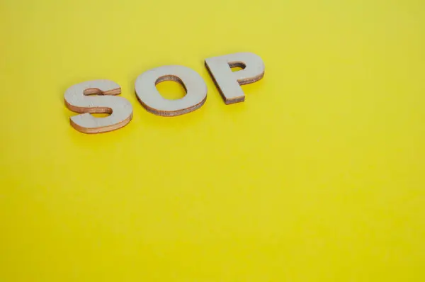 SOP wooden letters representing Standard Operating Procedures on yellow background.