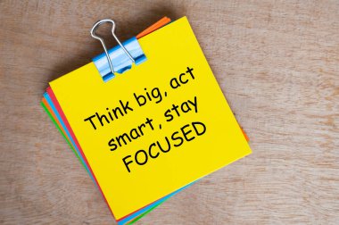 Think big, act smart, stay focused text on yellow notepad. clipart