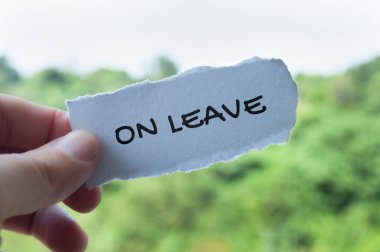 Hand holding torn paper with On Leave text with nature background. Annual leave concept. clipart