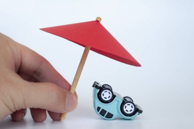 Red toy umbrella and upside down blue toy car on white background. clipart
