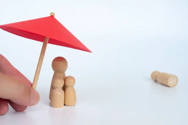 Family wooden dolls covered with toy umbrella representing life insurance and family protection.