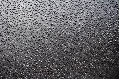 Koyu örtülü arka planda yağmurlu bir günün ardından berrak su damlalarının görüntüsü.